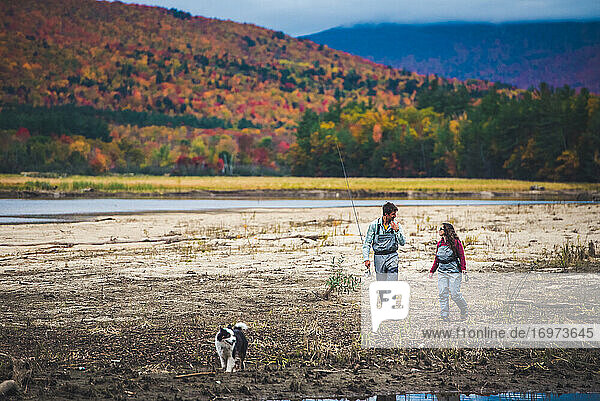 Male and female anglers walk down the shore with dog and foliage