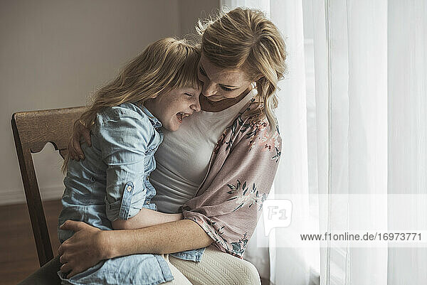 Mother and daughter laughing close together in natural light studio