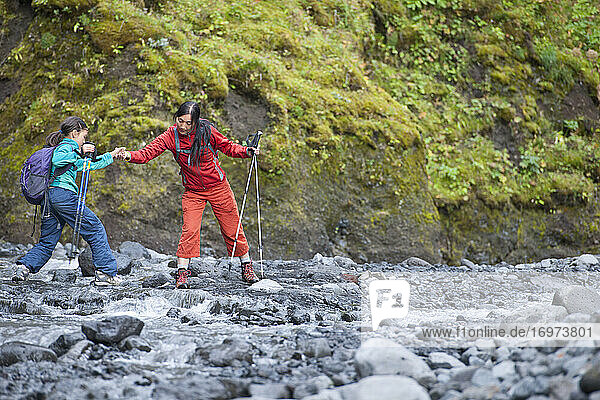 Mutter hilft ihrer Tochter beim Sprung über einen Fluss in Island