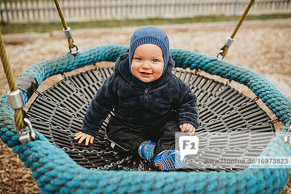Baby-Junge trägt blau in Spielplatz Nest Hängematte lächelnd im Winter