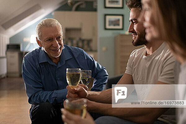 Cheerful senior man drinking wine with young couple