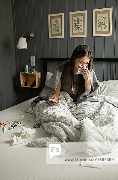 Kranke Frau mit Smartphone niesend auf dem Bett