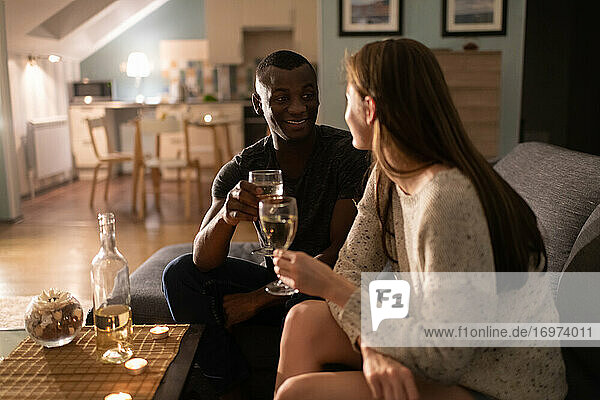 Fröhlicher schwarzer Mann trinkt Wein mit Freundin auf dem Sofa
