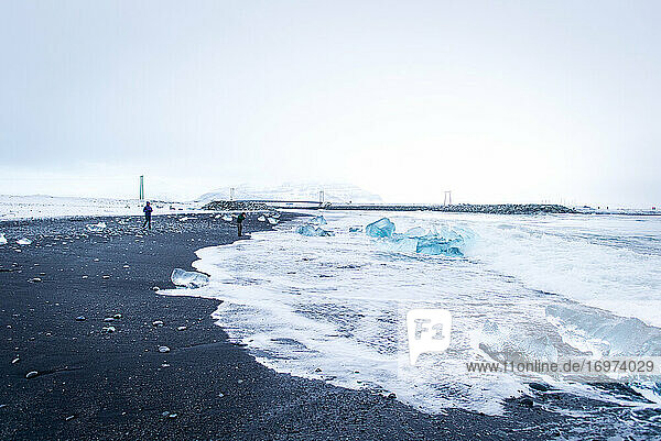 Zwei Personen erkunden den schwarzen Sandstrand Diamond Beach in Island im Winter