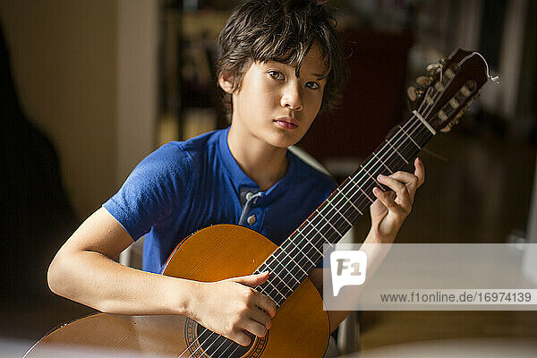 Ein Junge mit direktem Blick und ernster Miene hält eine klassische Gitarre