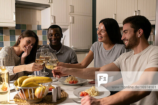 Multiethnische Freunde stoßen beim Abendessen mit Weingläsern an