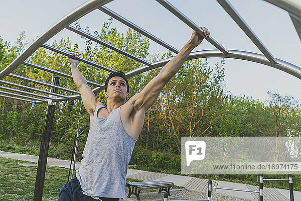 Young man doing pull-ups on monkey bars during workout