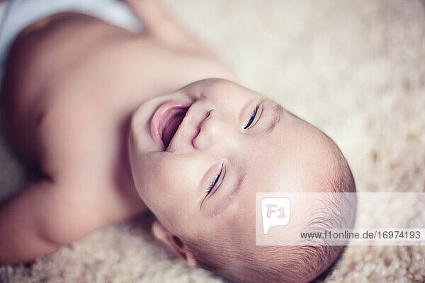 Baby boy laying on carpet and laughing at the camera with eyes closed.