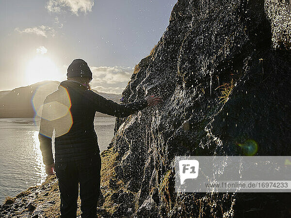 Frau berührt Wasser  das über Felsen fließt  auf den Färöer Inseln
