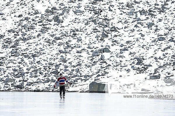 Junger Eishockeyspieler in Uniform  der den Puck mit dem Schläger manövriert  während er auf dem Eis eines zugefrorenen Sees in der Nähe eines mit Schnee bedeckten steinigen Berghangs in British Columbia  Kanada  fährt
