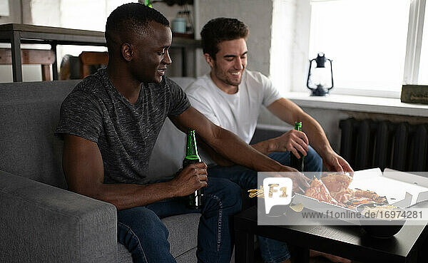Lächelnde Freunde  die während eines Fußballspiels Pizza und Bier genießen