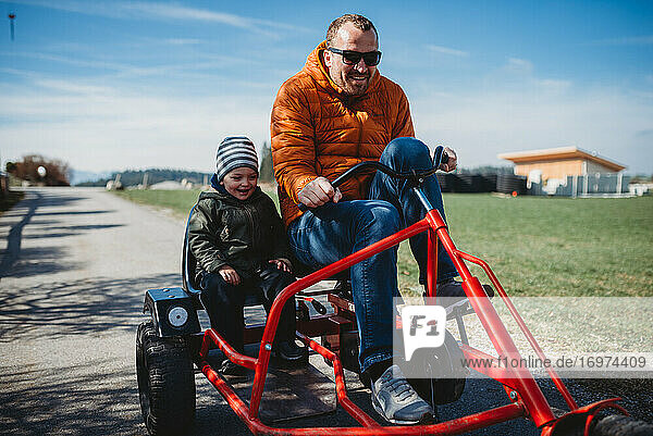 Vater und Sohn lächelnd und haben Spaß beim Fahren eines Wagens in einem Park im Winter