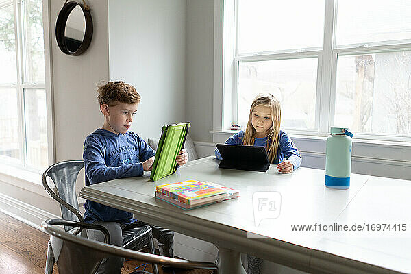 children siblings working on tablets together indoors at kitchen table