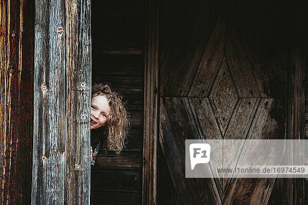 Adorable blonde girl playing hide and seek hiding in old wooden house