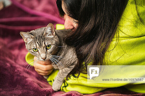 Nahaufnahme einer Frau  die ihre Katze auf einer lila Decke umarmt