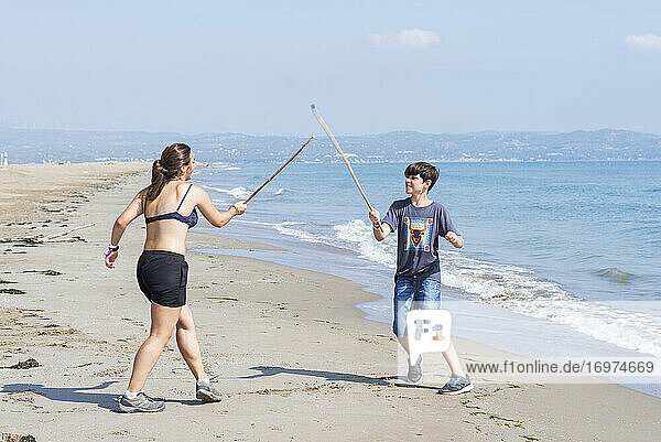 Zwei junge Freunde spielen mit Holzschwertern am Meeresstrand