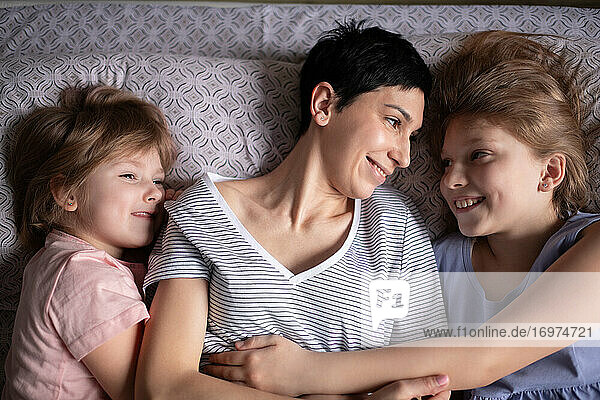 Glückliche Mutter umarmt Töchter im Bett am Morgen