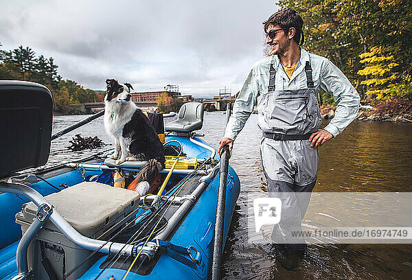 Mann hält sich an einem Boot im Fluss fest  Hund im Boot schaut zurück