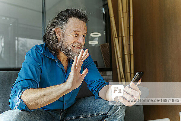 Älterer Mann mit Bart sitzt auf einem Sofa und schaut auf sein Smartphone