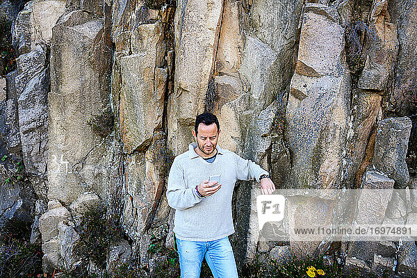 Bearded man standing against rock formation  holding mobile phone