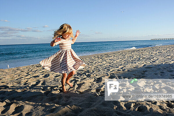 kleines Mädchen tanzt am Strand mit blauem Himmel