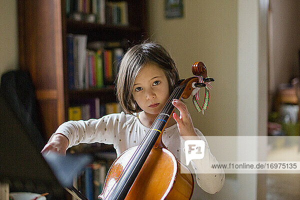 Ein ernsthaftes kleines Mädchen übt zu Hause bei schönem Licht Cello