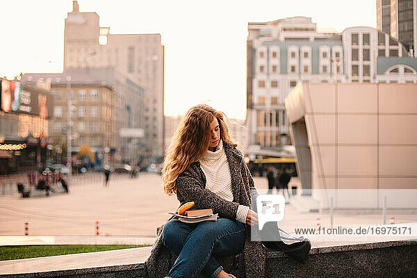 Teenage student girl looking in bag while sitting at campus in autumn