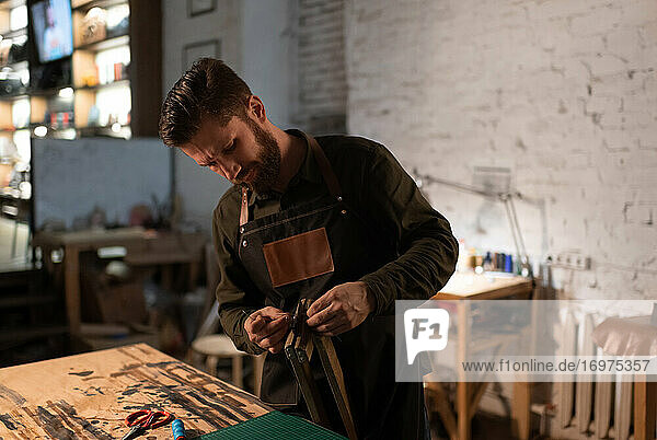 Bärtiger Handwerker beim Zusammenbau der Ausrüstung in einer Lederwerkstatt
