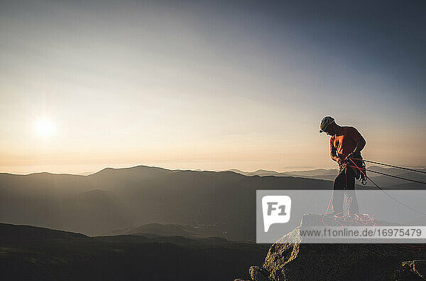 Mann beim Sichern mit Kletterseilen bei Sonnenaufgang in den Bergen