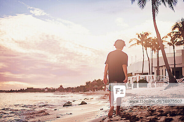 Pre teen boy walking on a tropical beach at sunset.