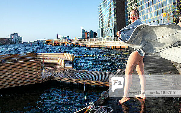 Frau hält Bademantel offen an einem windigen Wintertag nach dem Schwimmen in Kopenhagen