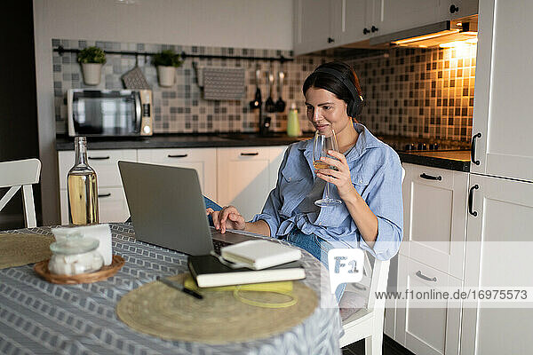 Frau trinkt Wein und benutzt Laptop in der Küche