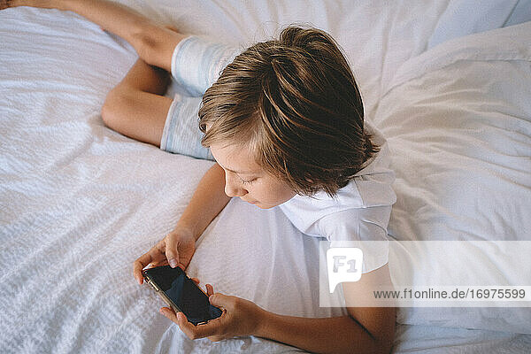 Junge in Weiß prüft sein Telefon vom Hotelbett aus.