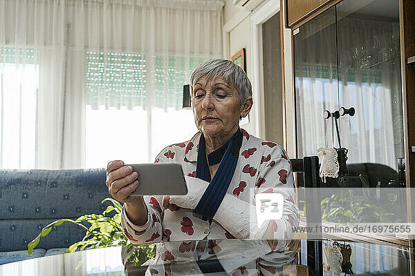 Weiße  weißhaarige ältere Frau mit gebrochenem Arm  die zu Hause sitzt