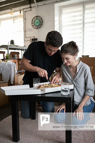 Junges Paar schneidet Pizza während des Umzugs