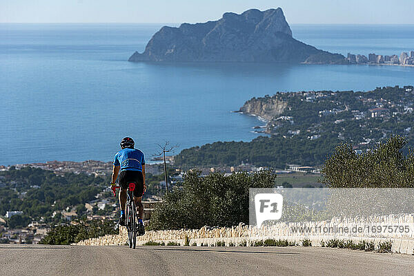 Cyclist going down Cumbre del Sol hill with view of mediterranean sea.