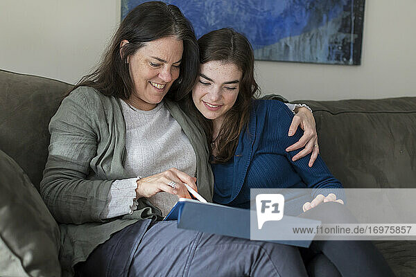 Mother with arm around teen daughter smiling and looking at tablet