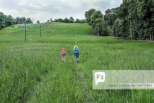zwei Mädchen gehen in der Ferne auf einen großen Hügel beim Wandern im Frühling