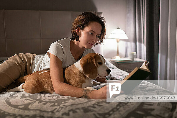 Junge Frau mit Beagle  die auf dem Bett ein Buch liest