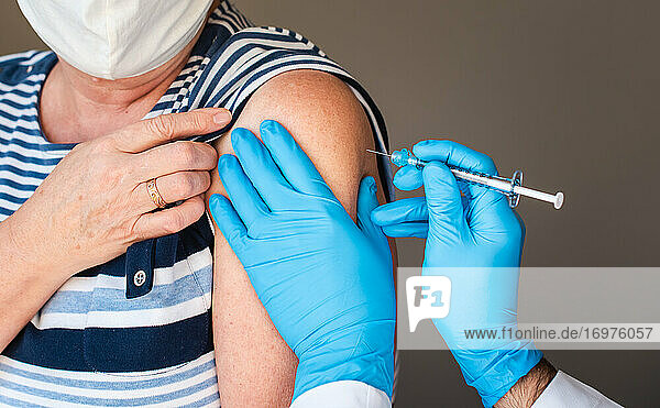 Nahaufnahme einer älteren Frau  der ein Impfstoff in den Oberarm injiziert wird.