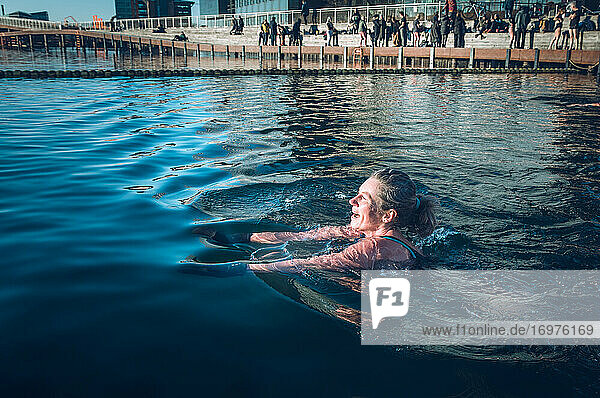 Mature Woman Swimming With Sun Shining In Freezing Water in Denmark