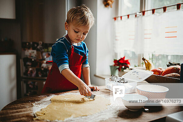 Young child making Christmas cookies in the kitchen at home with apron