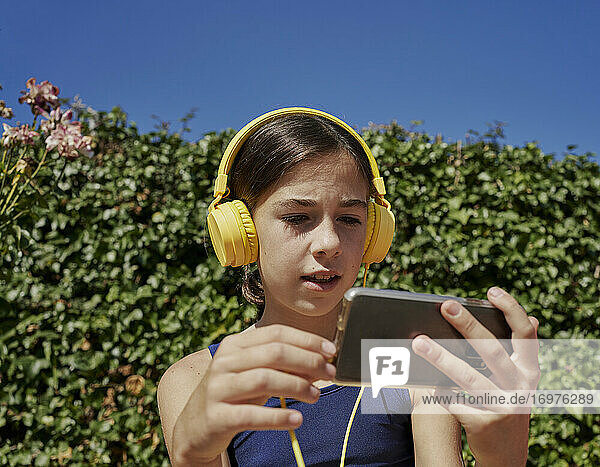 Schönes Mädchen hört Musik mit gelben Kopfhörern und hält ein mobiles Gerät