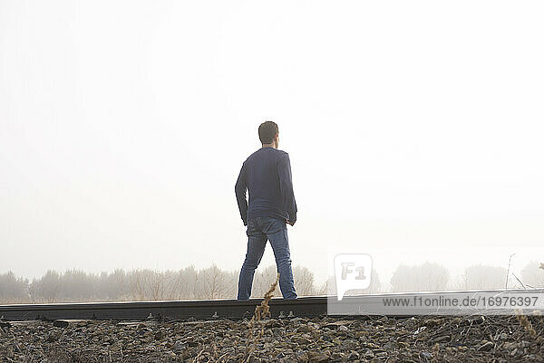Man in dense fog are walking along the railway tracks.