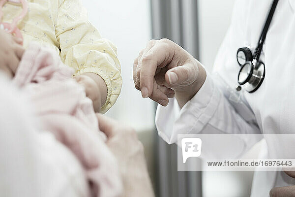 eine junge Ärztin hält ihre Hand an ein Kind in den Armen seiner Mutter