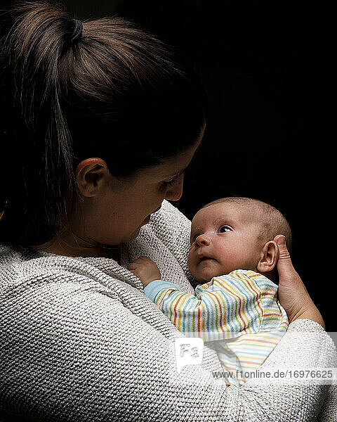 Liebevolle Mutter hält winziges Neugeborenes  während das Kind staunend nach oben schaut