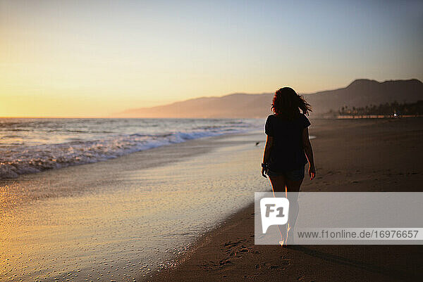 Junge Frau geht bei Sonnenuntergang am Strand spazieren