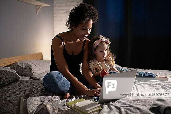 Ethnische Mutter mit Laptop für die Arbeit in der Nähe spielen Tochter