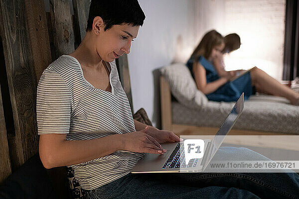 Mother working on laptop near daughters in evening