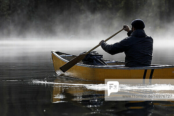 Konzentrierter Mann paddelt Kanu in den Nebel auf einem ruhigen See